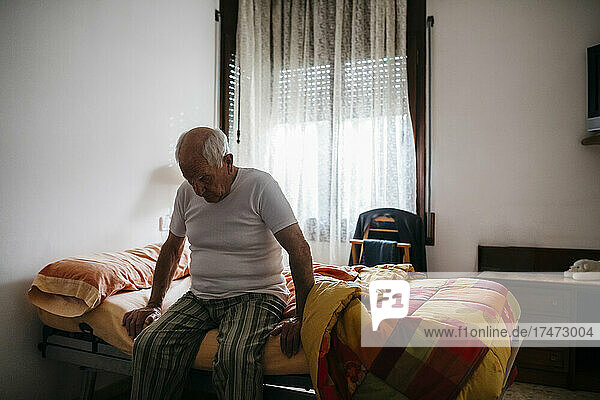 Lonely senior man sitting on bed at home