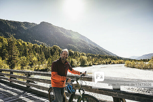 Smiling man wheeling bicycle on bridge