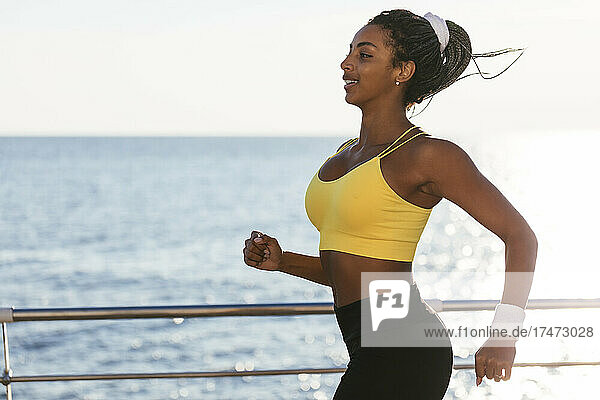 Female athlete jogging by sea during sunny day