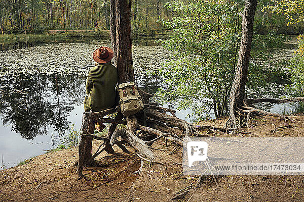Frau blickt auf den See  während sie neben einem Baum im Wald sitzt
