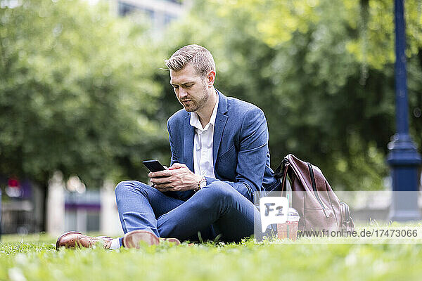 Male professional text messaging through mobile phone while sitting at park