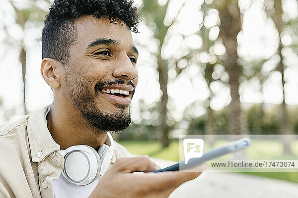 Lächelnder Mann mit kabellosen Kopfhörern  der über den Lautsprecher seines Smartphones spricht