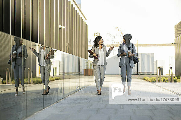 Female professionals talking while walking on footpath