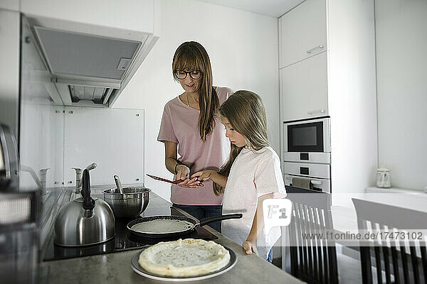 Daughter learning to cook from mother in kitchen