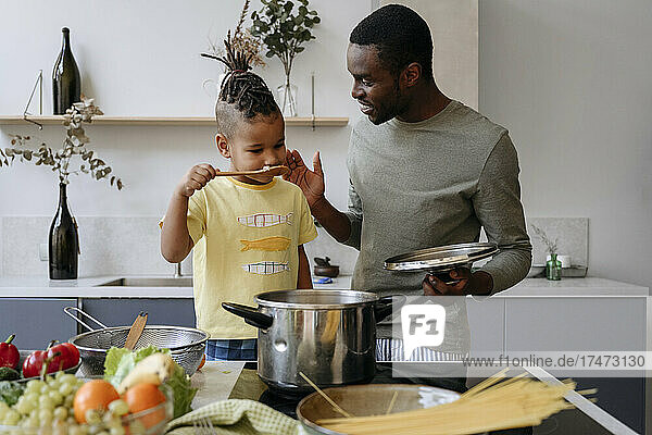 Young man talking with son smelling spaghetti in kitchen