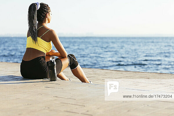 Young sportswoman sitting on footpath while looking at sea