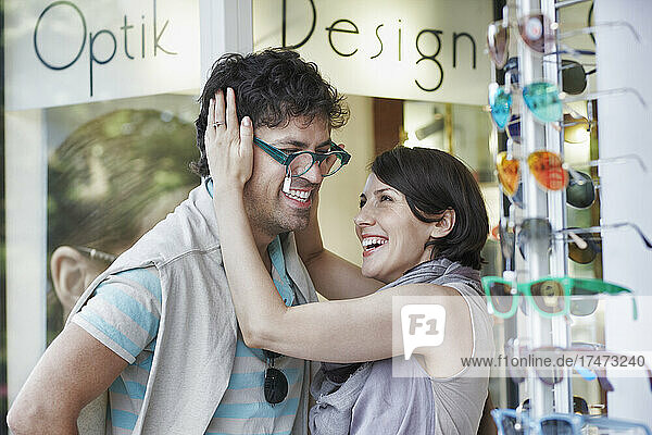 Happy woman trying eyeglasses on boyfriend at store