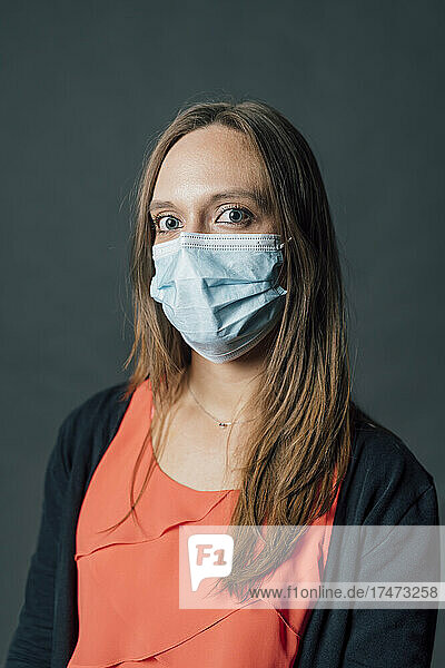 Woman with brown hair wearing protective face mask against gray background
