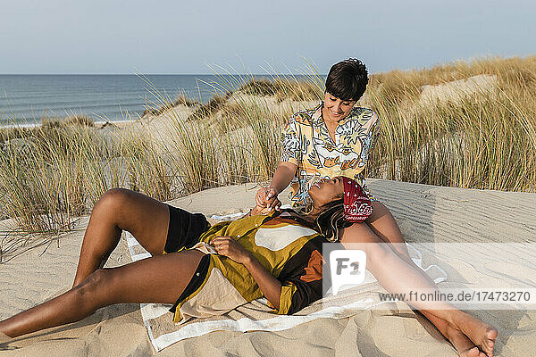 Lächelndes lesbisches Paar entspannt sich auf einer Picknickdecke am Strand