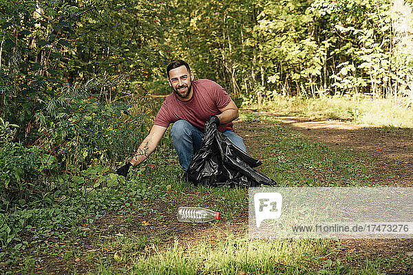 Smiling male environmentalist collecting garbage in forest