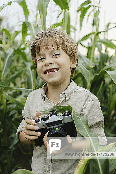 Smiling boy standing with vintage camera in corn field