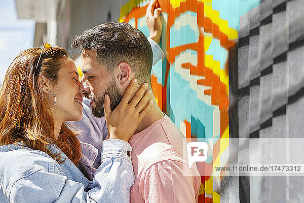 Couple kissing by grafitti wall during sunny day