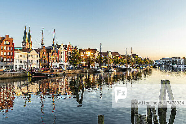 Germany  Schleswig-Holstein  Lubeck  Ships moored along river Trave canal at dusk with historic townhouses in background