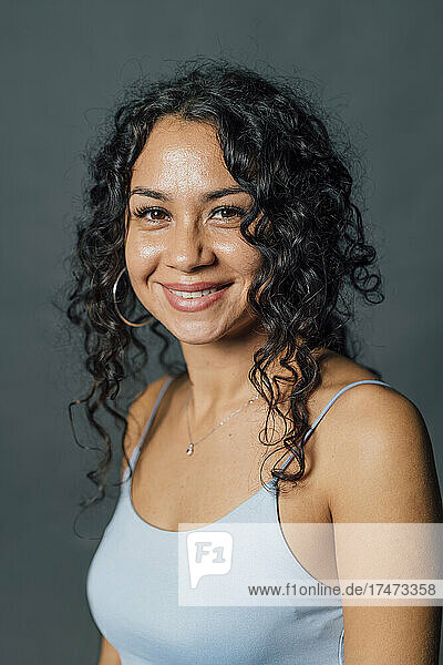 Smiling young woman with curly hair against gray background