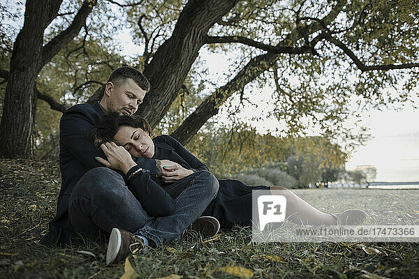 Loving couple relaxing on grass in front of tree