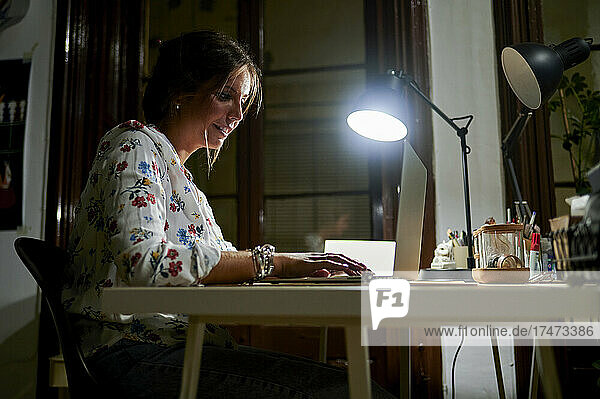 Businesswoman working on laptop by electric lamp in office during night