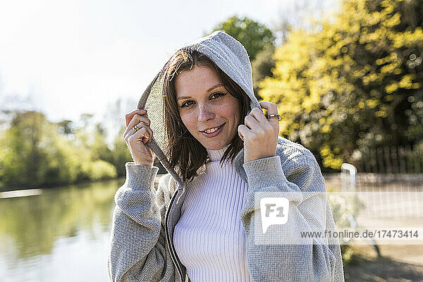 Woman holding jacket hood in park on sunny day