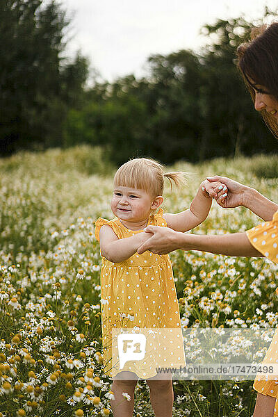 Cute daughter holding hands of mother on meadow