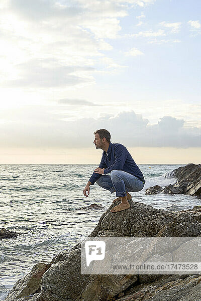 Man crouching on rock by sea at beach