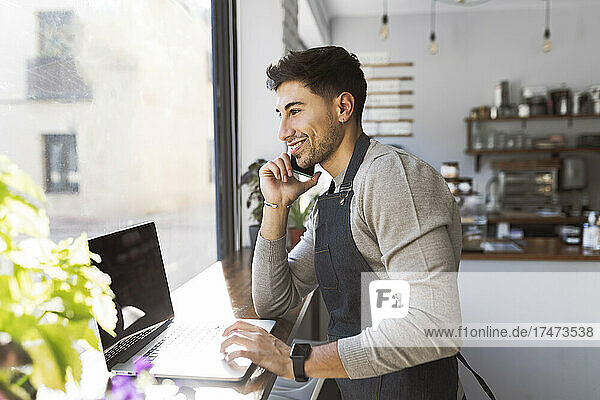Businessman wearing apron talking on mobile phone in coffee shop