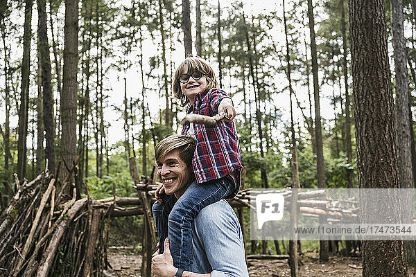 Smiling man carrying boy on shoulders at forest