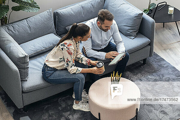 Businessman discussing over tablet computer with businesswoman on sofa