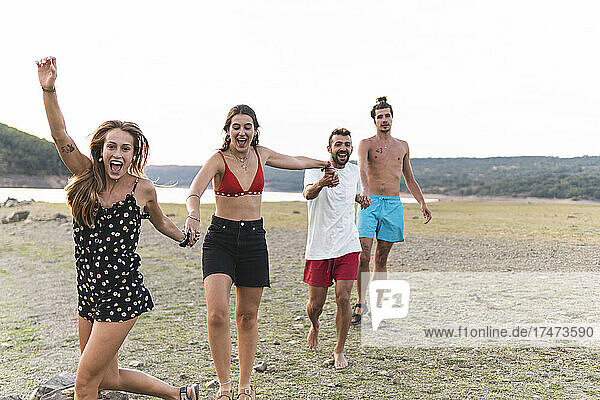 Fröhliche männliche und weibliche Freunde halten sich beim Spaziergang am Seeufer an den Händen