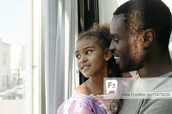 Smiling girl with father looking out of window at home