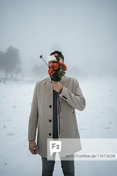 Mature man covering face with bunch of flowers during winter