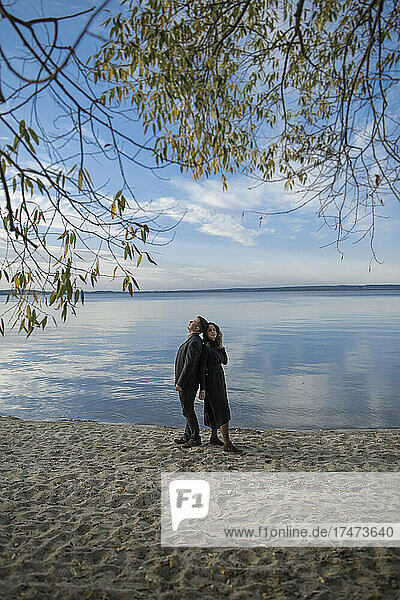 Paar steht Rücken an Rücken im Sand am Seeufer