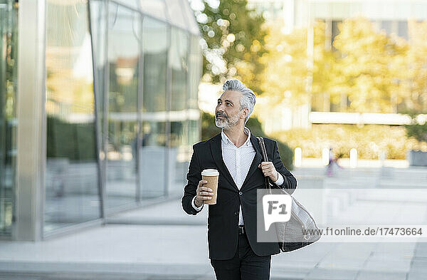 Businessman with bag and disposable cup outside office building