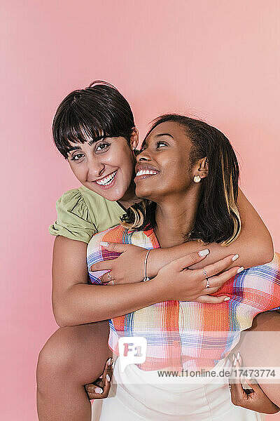 Frau trägt lesbische Freundin huckepack vor rosa Hintergrund