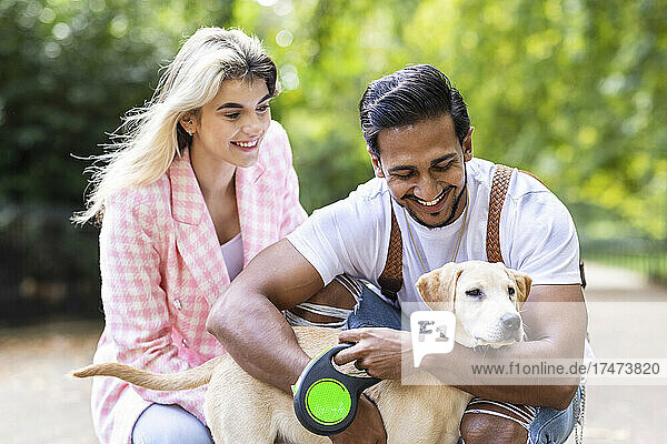 Smiling young man embracing dog by girlfriend in park