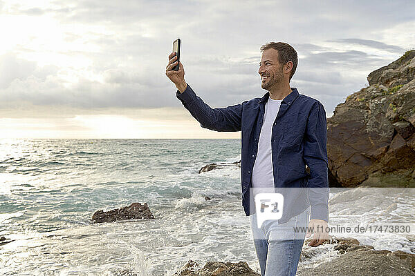 Smiling man taking selfie through smart phone at beach