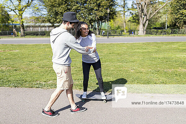 Man assisting friend while skateboarding in park
