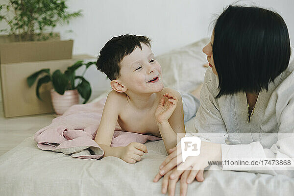 Smiling son talking with mother lying on bed in new house