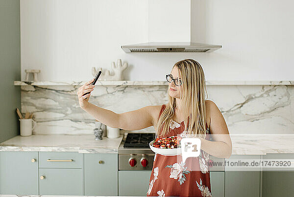 Female nutritionist with food taking selfie through smart phone in kitchen