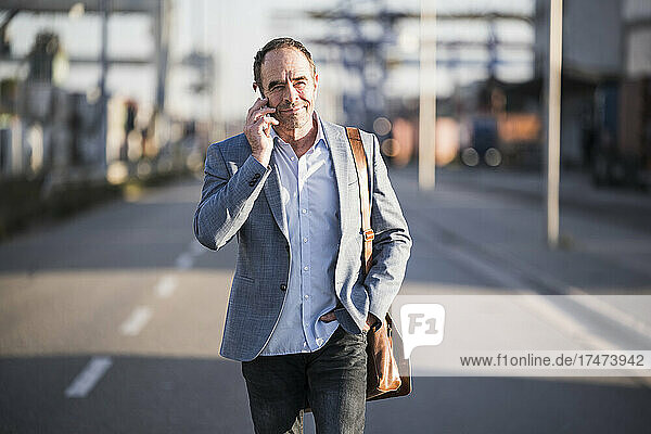 Reifer Geschäftsmann spricht mit Smartphone  während er auf der Straße geht