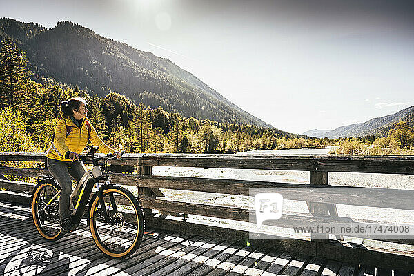 Woman cycling and looking at mountain on bridge