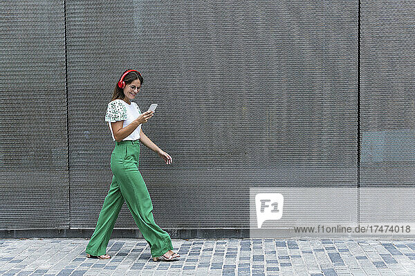 Smiling businesswoman listening music while using smart phone on footpath