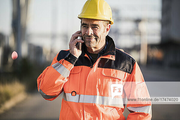 Mature male blue-collar worker talking over mobile phone at industry