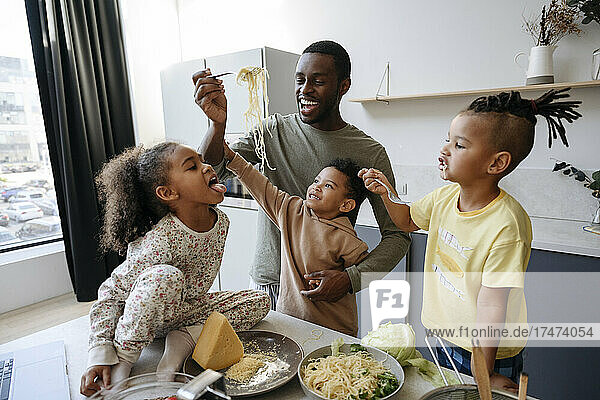 Happy man feeding spaghetti to daughter in kitchen