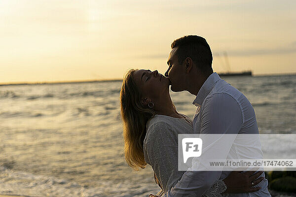 Freund küsst Freundin am Strand bei Sonnenuntergang