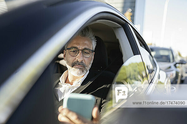 Geschäftsmann schaut im Auto auf sein Smartphone