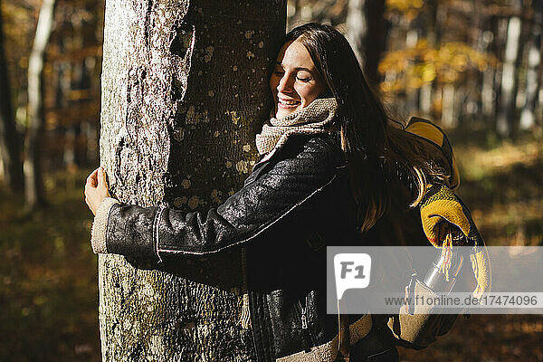 Happy young woman hugging tree in autumn forest