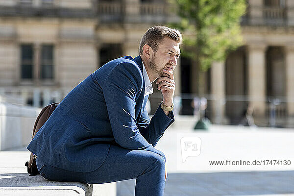 Businessman sitting with hand on chin on sunny day