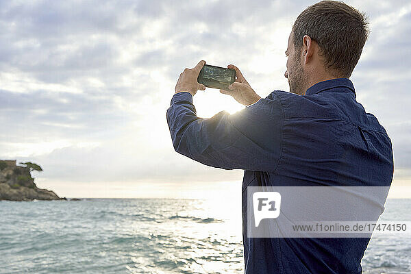 Man photographing sea through smart phone at beach
