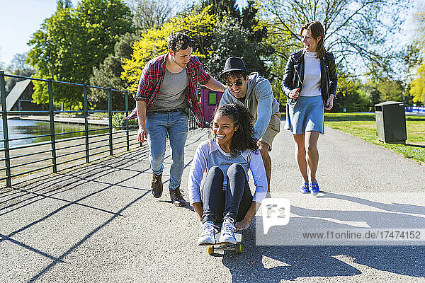 Friends playing with woman sitting on skateboard in park