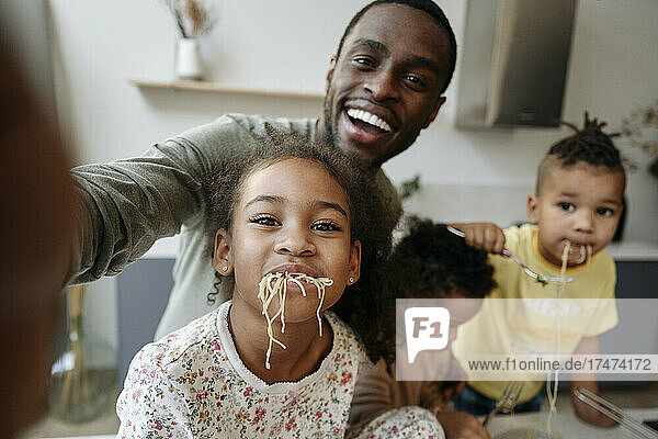 Glücklicher Mann macht ein Selfie mit Tochter und Söhnen  die in der Küche Spaghetti essen
