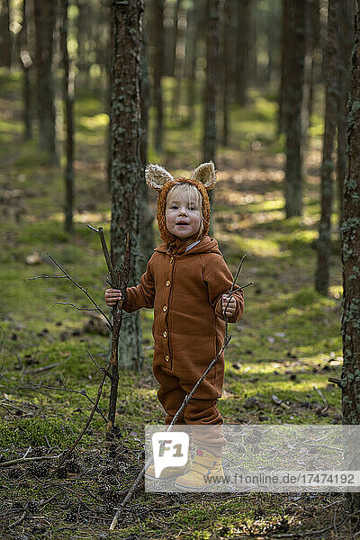 Smiling girl holding sticks in forest